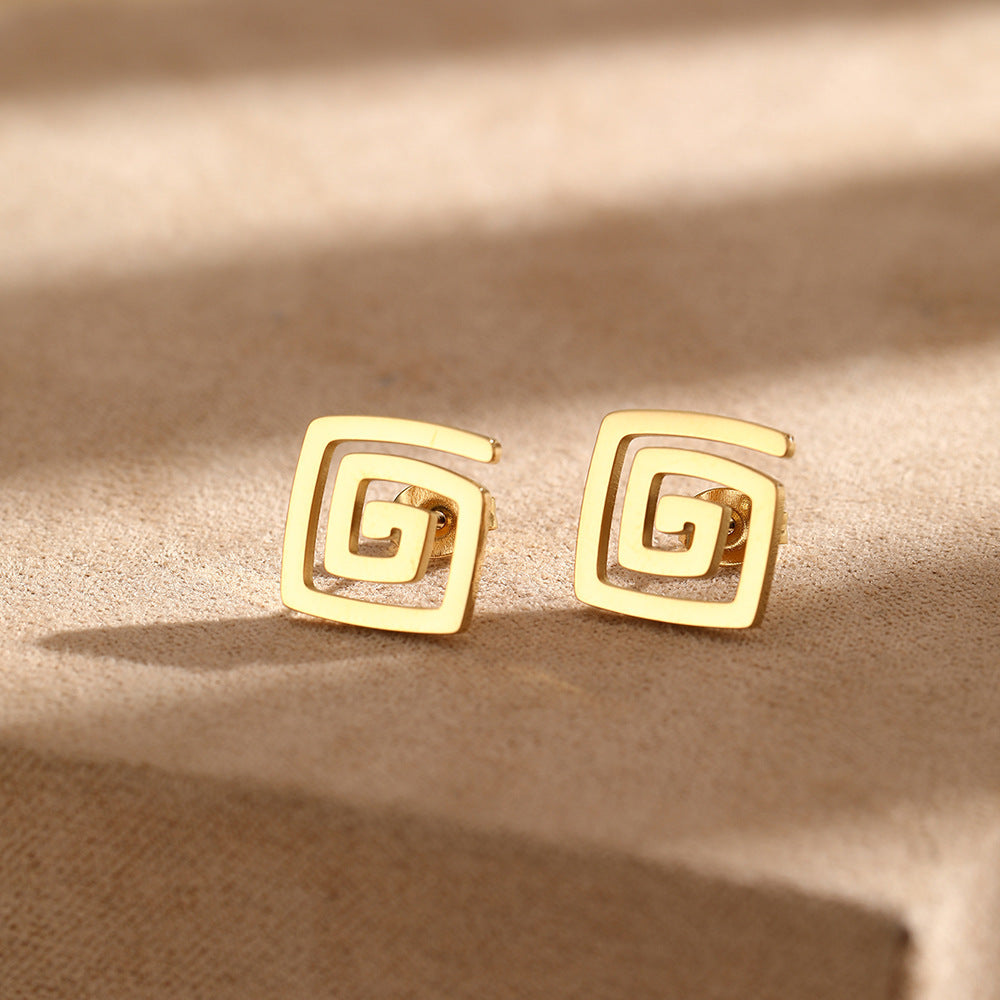 A pair of gold-plated stainless steel spiral square stud earrings resting on a neutral surface.