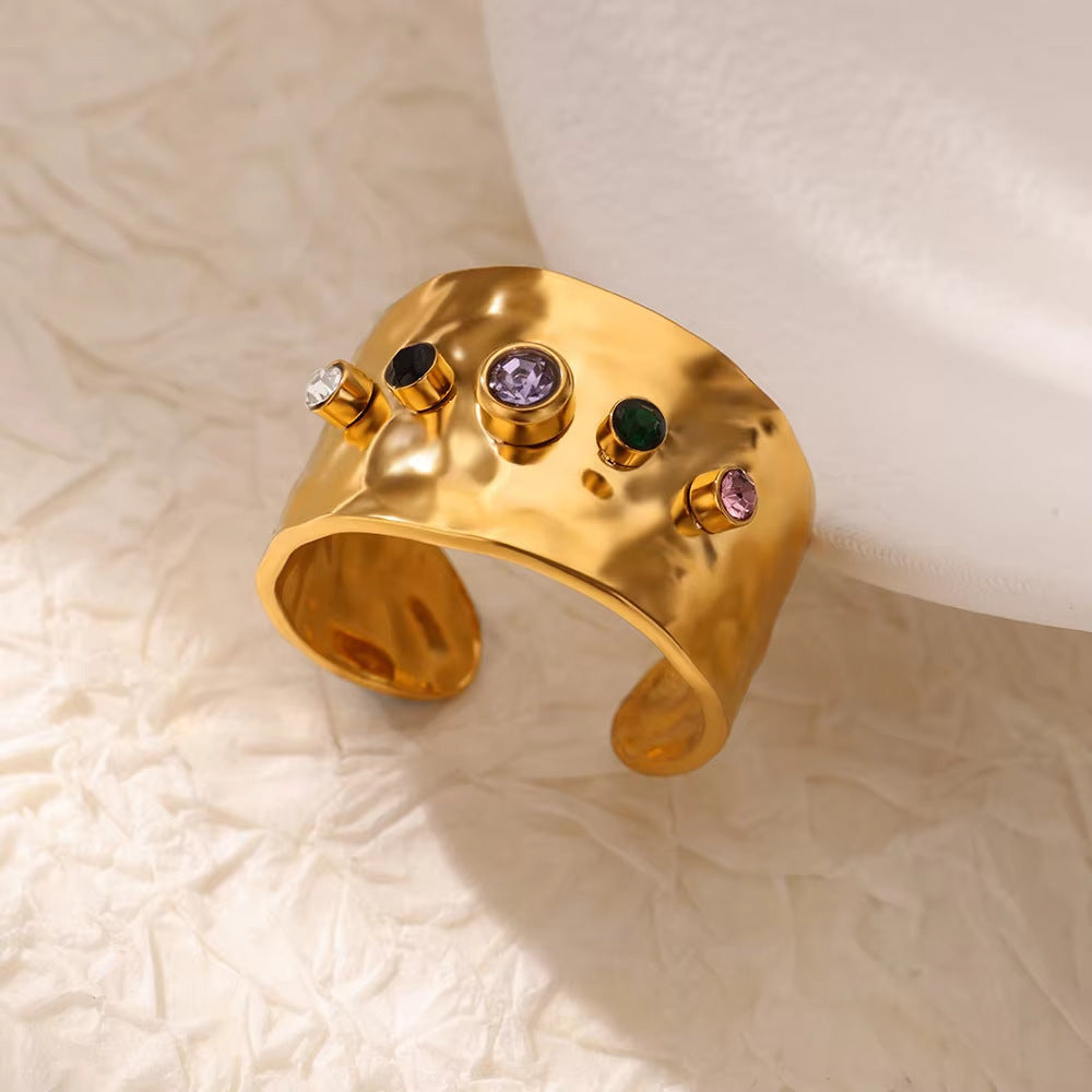 Wide gold open ring featuring an organic hammered texture and a row of multi-colored crystal accents.