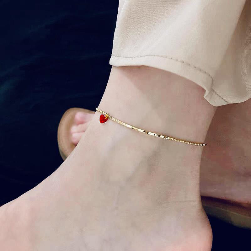 Gold chain anklet featuring a small red heart charm