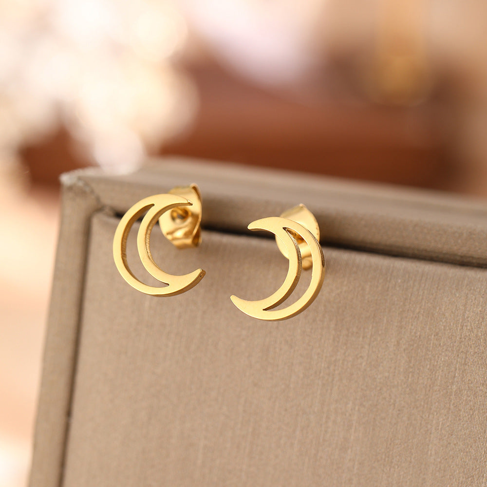 A pair of gold-toned hollow crescent moon stud earrings resting on a neutral surface.