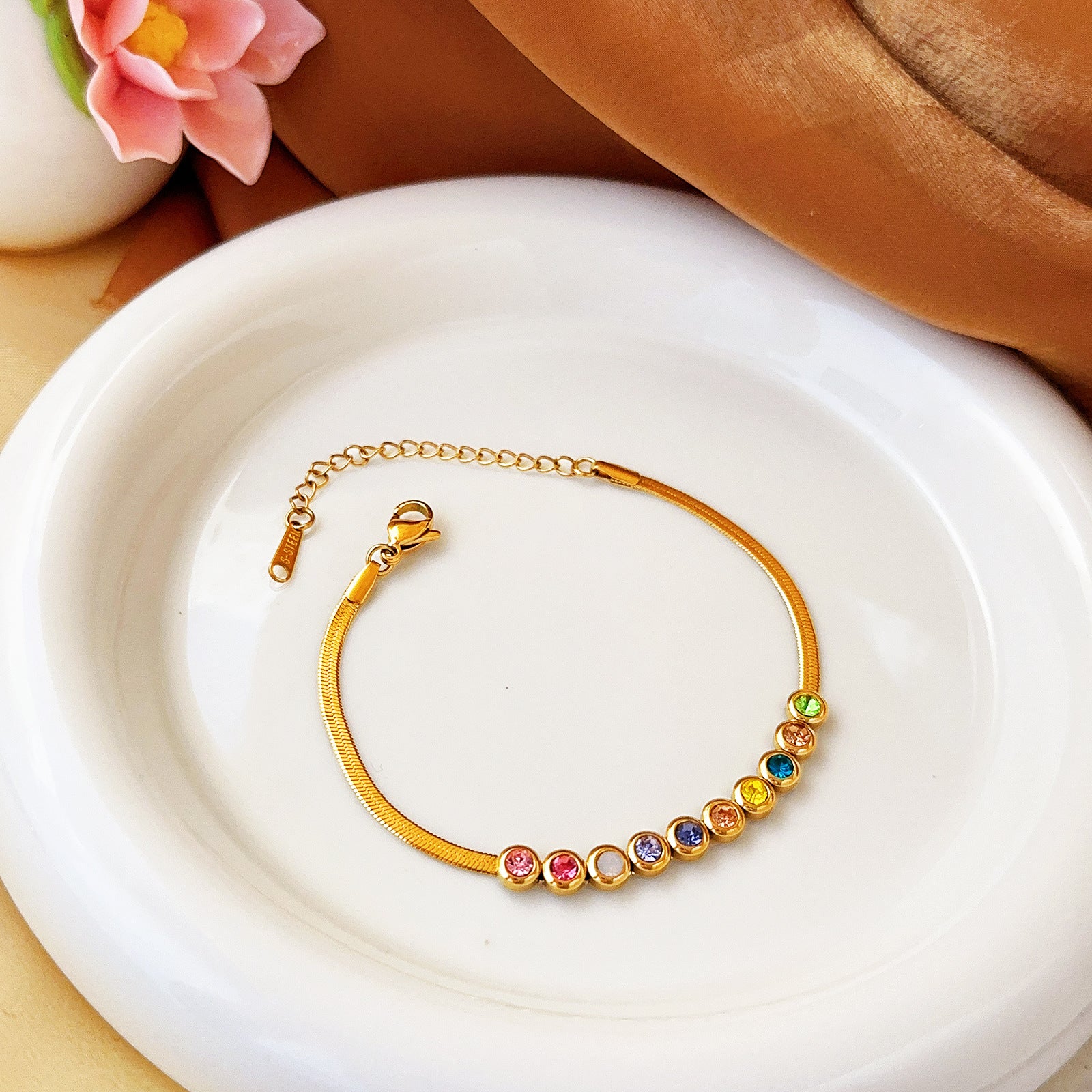 Gold tone herringbone chain bracelet featuring a row of multicolored bezel-set crystals and an adjustable clasp.