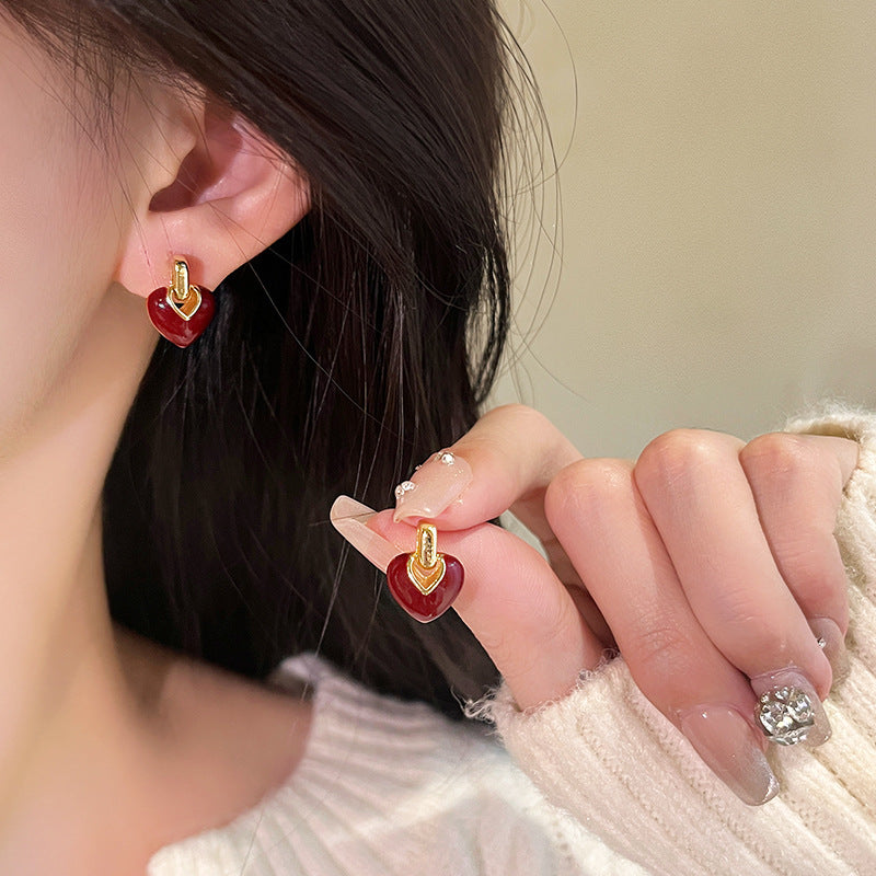 A pair of gold earrings featuring a red enamel heart suspended from a geometric top piece