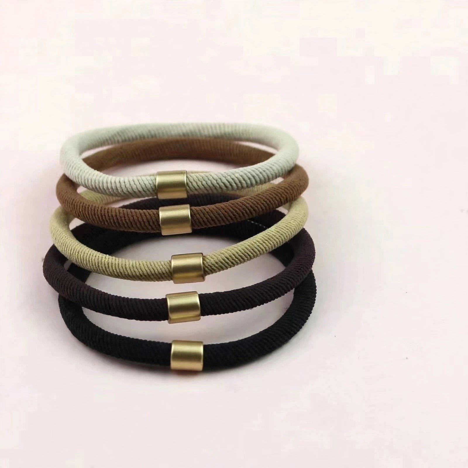 Stack of seamless cord hair ties with gold-tone clasps in neutral shades