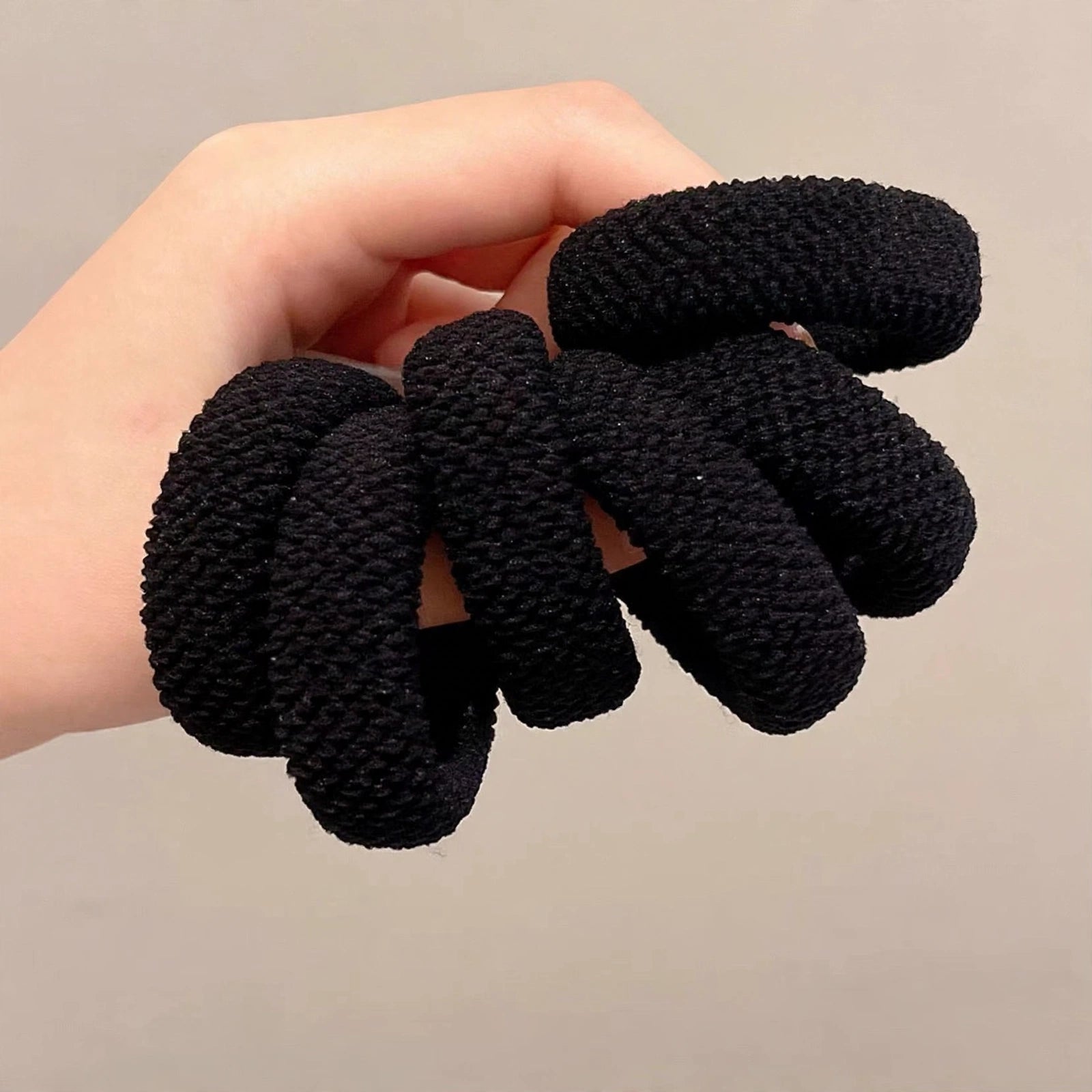 Hand holding a set of thick black seamless hair ties
